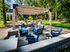 Shore Acres Apartments in Indianapolis, IN - Inviting outdoor seating area with modern pergola and stylish blue furniture, surrounded by lush greenery.