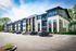 Shore Acres Apartments in Indianapolis, IN - Modern apartment complex with sleek architectural design, large windows, and ample parking set against a vibrant backdrop of trees and blue sky.