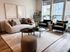 Sleek and modern living room with a cozy sofa, stylish armchairs, and natural light from large windows.