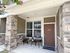 Inviting apartment entrance with a cozy patio featuring two stylish chairs and a small table, framed by rustic stone pillars.