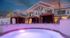 Elegant apartment complex with illuminated pool and stylish cabanas against a dramatic twilight sky.
