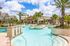 Luxurious apartment community pool with palm trees, sun loungers, and vibrant blue water.