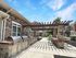 Elegant outdoor patio with built-in grills beneath a wooden pergola, surrounded by lush greenery.
