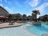 Luxurious outdoor pool area with palm trees and modern apartments under a clear blue sky.