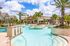 Inviting resort-style swimming pool with palm trees, sun loungers, and vibrant landscaping under a bright blue sky.