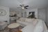 Modern living room with cozy beige sectional, stylish coffee table, and an inviting open-concept kitchen. Elegant decor includes a classic wall clock and artistic horse painting.