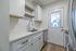 Contemporary kitchen with sleek white cabinetry, modern stainless steel appliances, and elegant wood flooring leading to a bright back door.