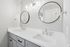 Elegant bathroom with modern dual sinks and chic round mirrors, featuring sleek gray cabinetry and stylish lighting.