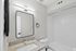 Modern bathroom featuring a sleek granite countertop, elegant square mirror, and pristine white tile shower.