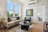 Bright and inviting living room with modern decor, featuring a cozy beige sofa, large windows, and contemporary artwork, perfect for relaxing.