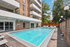 Cheesman Park, CO, apartments near Bluebird Theatre - The Grove on York - Outdoor Swimming Pool With Lounge Chairs, Sun Deck, and Surrounding Apartment Building Balconies Under a Clear Blue Sky.