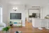 Contemporary apartment interior with open-plan living room and kitchen, featuring sleek white cabinetry, modern appliances, and stylish bar stools for a chic, inviting space.