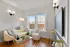 Bright and cozy living room with chic white furniture, elegant lighting, hardwood floors, and large windows offering city views.