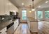 Bright and modern kitchen with granite countertops, stainless steel appliances, and elegant pendant lighting opening into a spacious living area with large windows and hardwood flooring.