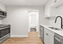 Sleek modern kitchen with stainless steel appliances, elegant white cabinetry, and chic wood flooring, leading to a bright bathroom.