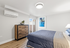 Bright and modern bedroom featuring a cozy bed, stylish wooden dresser, and contemporary artwork, with abundant natural light from the sliding glass door.