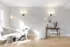 Bright and elegant living room with a cozy white sofa, modern lighting, and artistic decor on a wooden floor.
