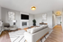 Elegant living room with modern decor, featuring a cozy sofa, stylish armchair, flat-screen TV above a white brick fireplace, and bright wooden flooring.