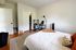 Inviting bedroom featuring a cozy bed, modern desk setup, and ample natural light, perfect for rest and productivity.