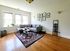 Bright living room with a modern gray sectional sofa, artistic wall decor, and a vibrant patterned rug on hardwood flooring, filled with natural light from large windows.