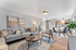 Elegant open-plan living room with modern decor, plush gray sofa, chic wooden furniture, and a bright, airy kitchen in the background.