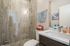 Modern bathroom with glass shower, elegant stone tiles, and a sleek vanity with ample lighting.