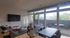 Bright and modern living room with large windows, cozy seating, and sleek dining area opening to a private balcony with scenic views.