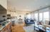 Bright and inviting living room with open concept kitchen, featuring elegant furnishings, hardwood floors, and expansive windows with a balcony view.