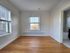 Bright and airy room with elegant hardwood floors, large windows for natural light, and a glimpse of a modern bathroom.