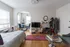 Charming studio apartment featuring a cozy sleeping area, stylish arched dining nook with blue chairs, and a modern living space ideal for relaxation.