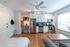 Bright and modern studio apartment with an open-plan kitchen and living area. Features sleek stainless steel appliances, white cabinets, and warm hardwood floors complemented by ample natural light.
