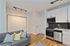 Modern apartment kitchen with sleek cabinetry, stainless steel appliances, and cozy living room area featuring a stylish grey sofa and patterned cushions.