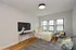Inviting and bright bedroom with modern decor, featuring a cozy bed, stylish sofa, and wall-mounted TV, highlighted by natural light from large windows and elegant wooden flooring.