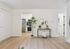 Chic apartment entrance with elegant wooden flooring, stylish console with mirrors, and a glimpse into a modern kitchen, exuding warmth and contemporary charm.