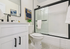 Modern bathroom featuring sleek black fixtures, elegant white cabinetry, and a stylish glass-enclosed bathtub.