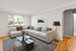 Bright and inviting living room with a modern sectional sofa, stylish floor lamp, and large window offering lush green views.