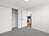 Bright bedroom with plush carpet, spacious closet, and a glimpse into a modern kitchen with sleek appliances.