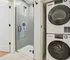 Sleek bathroom design featuring a modern glass shower with stylish tiled accents next to a convenient in-unit stacked washer and dryer.