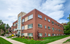Charming red-brick apartment building with manicured lawns and a modern glass entrance, perfect for urban living.