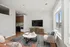 Bright and modern living room with a cozy seating area, flat-screen TV, and a stylish open kitchen in the background.