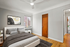 Bright and spacious bedroom with elegant d&eacute;cor, featuring a stylish bed, modern art, and a large window offering natural light.
