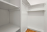 Spacious and elegant walk-in closet featuring built-in shelving and pristine white walls.