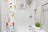 Bright bathroom with vibrant floral shower curtain, sleek modern fixtures, and elegant wall shelves for a fresh, inviting space.