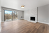 Bright and spacious living room featuring elegant hardwood floors, a cozy white brick fireplace, and large sliding glass doors opening to a scenic balcony.