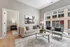 Modern living room featuring chic beige sofa, stylish armchairs, and expansive windows with city views, harmoniously blending contemporary design with urban elegance.
