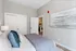 Elegant bedroom with cozy bedding, modern artwork, and a glimpse into a contemporary kitchen, perfect for stylish living.