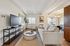 Bright and inviting living room with cozy beige sofa, modern armchair, and stylish decor, seamlessly connected to dining area with elegant chandelier.