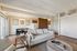 Bright and inviting living area with elegant decor, comfortable seating, and an open dining space. Sleek kitchen in the background with modern appliances.
