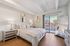 Elegant bedroom with a plush bed, modern artwork, and a large mirror reflecting natural light from a balcony view.