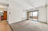 Bright living room with textured ceiling, sliding glass doors leading to a balcony, and a cozy kitchenette in view.